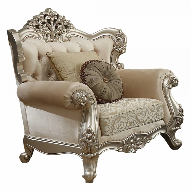 Champagne upholstered chair with wood leg trim and pillows against a studio couch and outdoor furniture setting