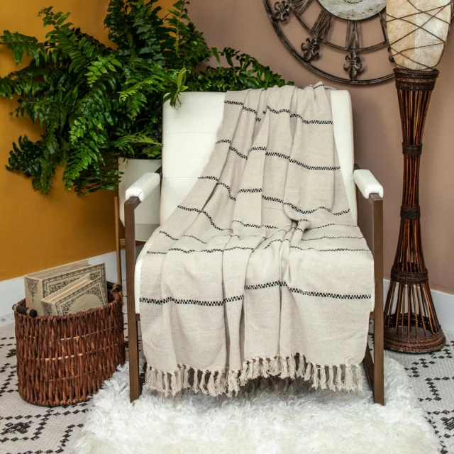 Beige handloom throw blanket with tassels in cozy interior with furniture and plants.
