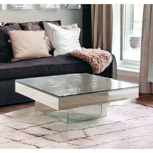 Clear silver glass mirrored coffee table in a modern interior design setting with pillows and grey accents