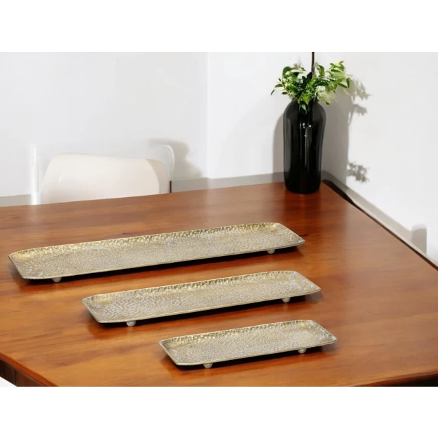 gold rectangular metal serving trays on wooden table with plants