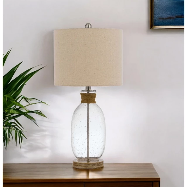 jar table lamp with brown drum shade next to plant on wooden table in interior design setting